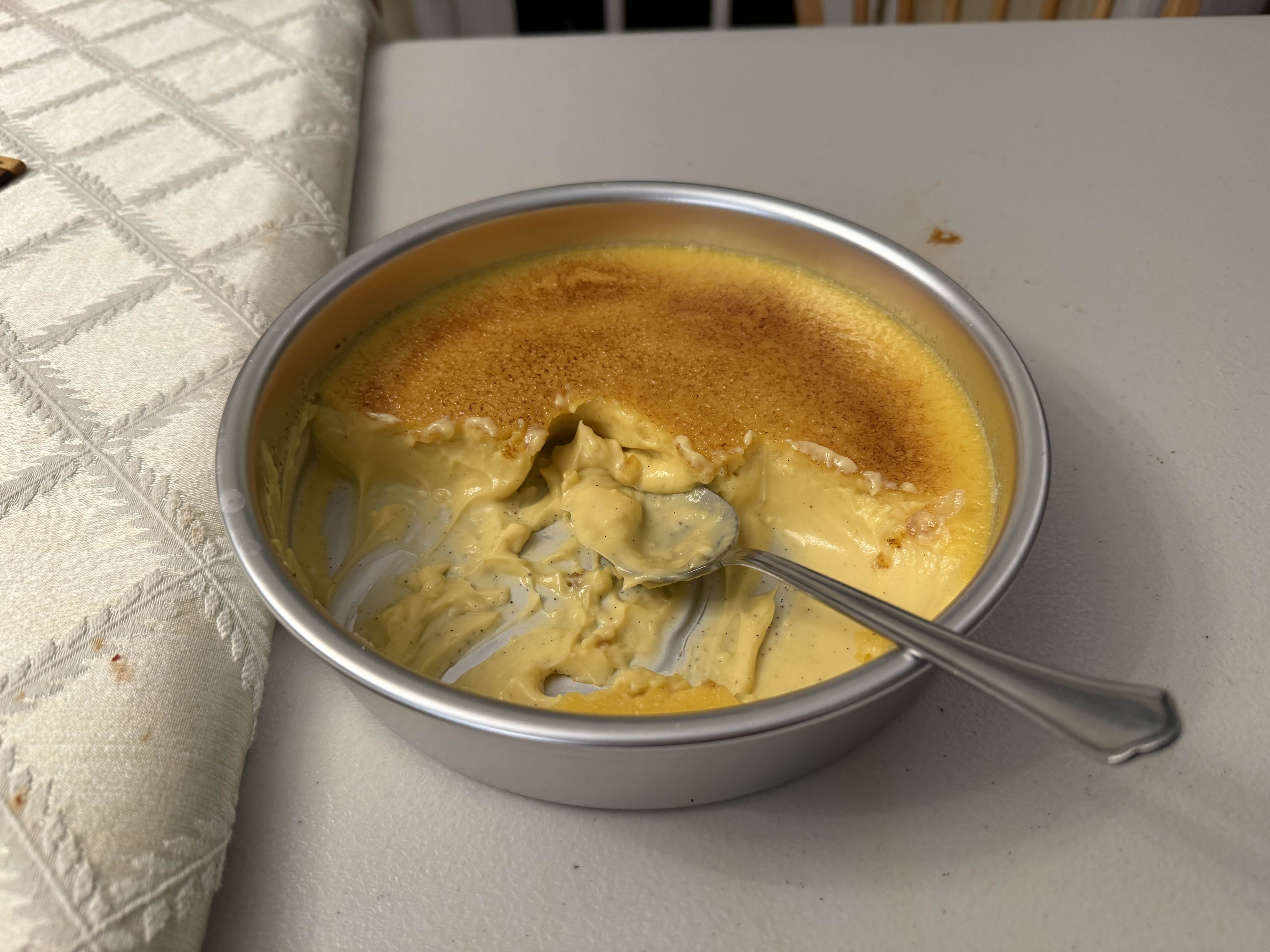 Half-eaten Creme brulee in a round aluminum cake pan